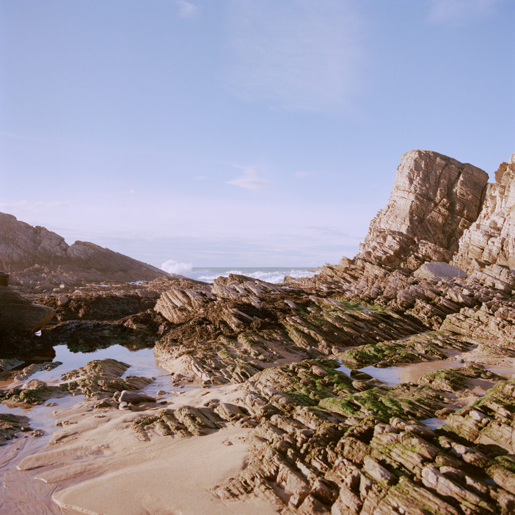 Craggy coastal rocks, sand, sea, blue sky